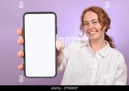 Ein positiver Millennials mit Smartphone und weißem, leerem Bildschirm auf farbenfrohem Studiohintergrund Stockfoto