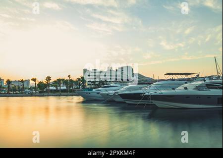 Eine Reihe von Booten, die bei Sonnenuntergang in Eilat, Israel, an einem Dock vor einer Reihe von Gebäuden festgemacht wurden. Stockfoto