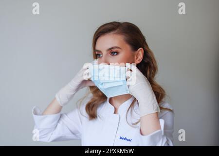 Junge, schöne Frau, die zeigt, wie man eine medizinische Maske trägt Stockfoto
