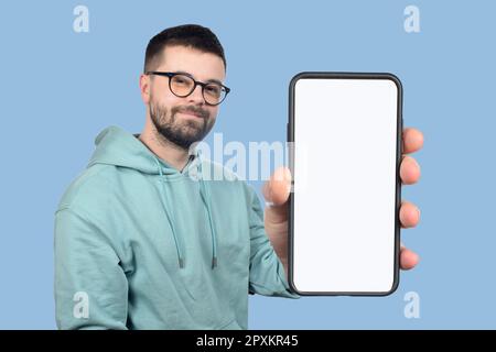 Ein junger Mann mit Brille und Bart zeigt ein Telefon mit einem leeren weißen Bildschirm Stockfoto