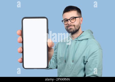 Ein junger Mann mit Brille und Bart zeigt ein Telefon mit einem leeren weißen Bildschirm Stockfoto