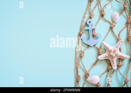 Schöner nautischer Hintergrund mit braunem Hanffischnetz, kleinem blauen Anker und elfenbeinfarbenen Seesternen auf aquamaringrünem Hintergrund Stockfoto