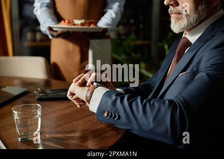 Nahaufnahme eines erwachsenen Mannes, der am Tisch sitzt und auf sein Mittagessen wartet, serviert vom Kellner im Café Stockfoto