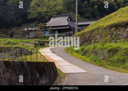Schmale Straße an einer alten Steinmauer zum traditionellen japanischen Haus im ländlichen Dorf Stockfoto