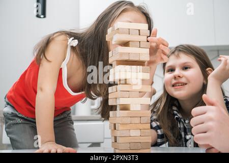 Eine Gruppe begeisterter Kinderspieler spielt Brettspiel Jenga auf dem Tisch in der Küche zu Hause, Bauturm aus Holzbalken. Brettspiele, Stockfoto