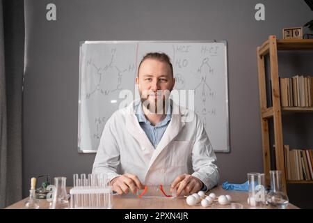 Porträtlehrer oder Tutor, der Online-Unterricht gibt, erklärt, im Klassenzimmer an einem hölzernen Schreibtisch sitzt. Stockfoto