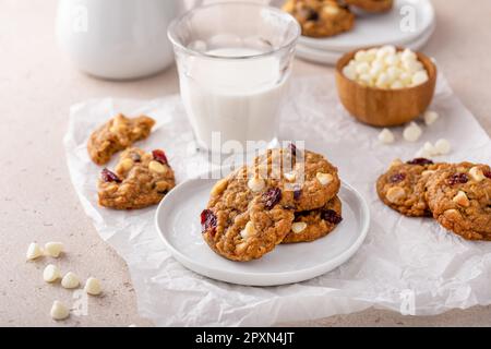 Weiße Schokolade und Preiselbeerkekse auf einem weißen Teller mit einem Glas Milch Stockfoto