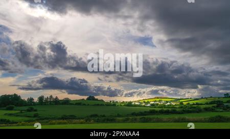 Himmel mit Kumuluswolken über einem irischen Dorf am Abend. Irische Siedlung im County Cork, dramatische Landschaft. Europäische Landschaft, rustikale Landschaft. Stockfoto