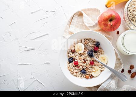 Eine Schüssel mit trockenem Müsli und Müsli serviert mit frischem Obst und Nüssen. Haferflockenplatte. Gesunde Ernährung, Ernährung. Draufsicht. Stockfoto