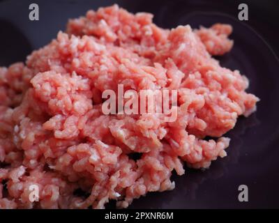 Hackfleisch auf einem großen lila Keramikteller. Köstliches frisches Hackfleisch für die Zubereitung von Koteletts, Steaks, Hamburgern und Fleischbällchen. Halbfertigerzeugnis aus Schweinefleisch Stockfoto