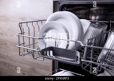 Vorderansicht der offenen automatischen Edelstahl-Einbaumaschine mit vollständig integrierter Steuerung der oberen Spülmaschine mit sauberen Utensilien, Besteck, Gläsern und DIS Stockfoto