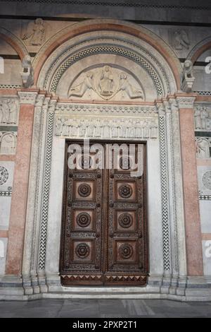 Eine antike Holztür mit komplexen Mustern und Designs befindet sich in einem hellrot gestrichenen Gebäude Stockfoto