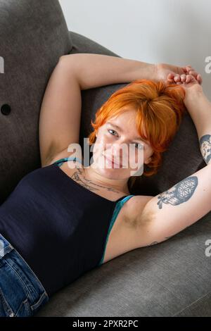 Eine Frau mit behaarten Achselhöhlen, die auf einem Sofa liegt, mit den Armen über dem Kopf. Stockfoto