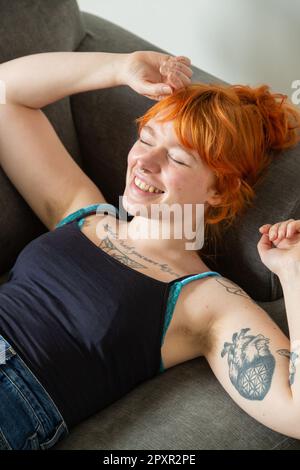 Eine Frau mit behaarten Achselhöhlen, die auf einem Sofa liegt, mit den Armen über dem Kopf. Stockfoto