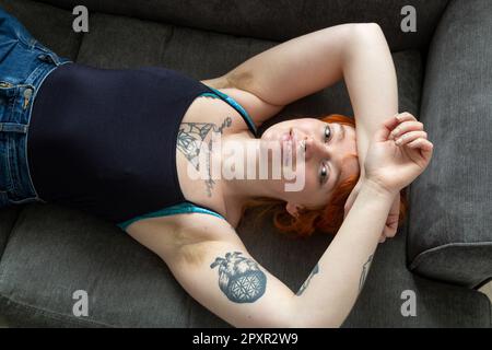 Eine Frau mit behaarten Achselhöhlen, die auf einem Sofa liegt, mit den Armen über dem Kopf. Stockfoto