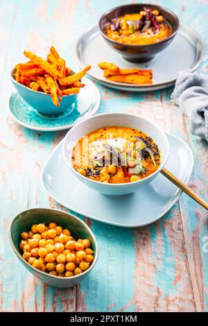 Karotten- und Süßkartoffelsuppe mit Kichererbsen und frischen Winterkräutern, Süßkartoffeln-Pommes Stockfoto