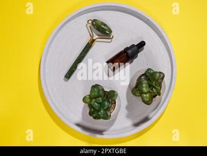 Handmassagegerät für das Gesicht und braune Glasflasche mit Pipette auf runder Platte, Draufsicht Stockfoto