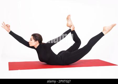 Hübsches, sportliches Mädchen im schwarzen Anzug, das Yoga macht. Naukasana asana Boot Pose. Isoliert auf weißem Hintergrund. Stockfoto