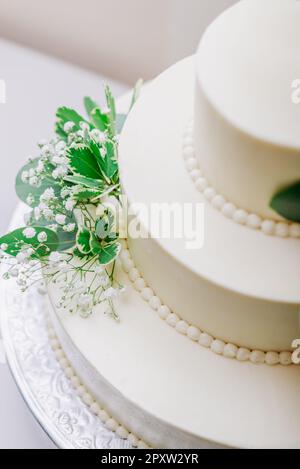 Dreistöckiger weißer Hochzeitstorte mit grünem Blumendekor. Stockfoto