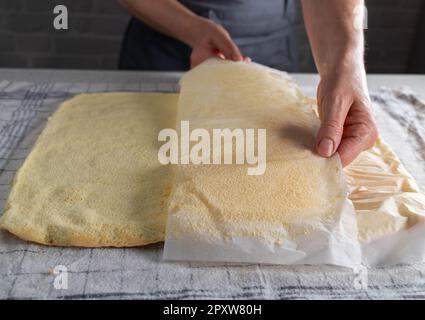 Backpapier von einem frisch gebackenen Schwammkuchen entfernen, um schweizer Brötchen mit der Hand einer Frau zuzubereiten Stockfoto
