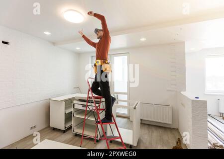 Elektriker repariert Deckenventilator mit Lampen im Innenbereich. Platz für Text. Stockfoto