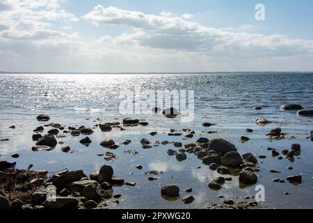 Große Steine liegen im Wasser an der Ostseeküste, mit Wellen und Horizont Stockfoto