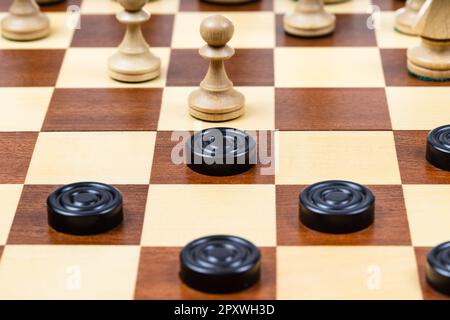 Spielen nach unterschiedlichen Regeln auf einem Spielbrett – schwarze und weiße Schachfiguren auf Holzschachbrett, Bauer und Schachbrett in der Mitte des Spielbretts Stockfoto