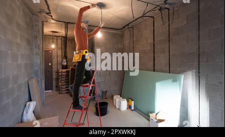 Elektriker repariert Deckenventilator mit Lampen im Innenbereich. Platz für Text. Stockfoto