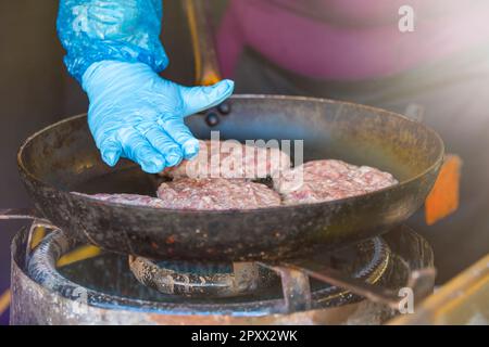 Die Hände des Kochs bereiten in einer Bratpfanne Schnittlauch aus Hackfleisch zu. Fast Food Restaurant auf der Straße. Stockfoto