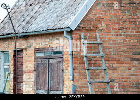 Eine Mauer aus Ziegelstein mit einer Leiter, die sich dagegen lehnt. Stockfoto
