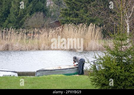 Ein Mann, der in einem See mit einem grünen Feld im Hintergrund angeln will. Stockfoto