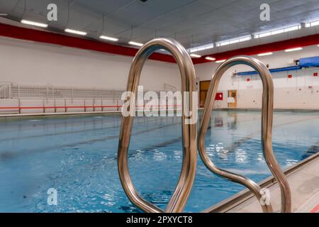 Edelstahl-Natatorium/Schwimmbadleiter mit Haltegriffen im öffentlichen Schwimmbad. Stockfoto