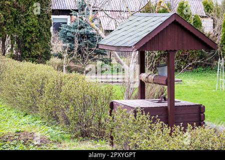 Ein hölzerner Brunnen mit grünem Dach befindet sich in einem Garten. Stockfoto