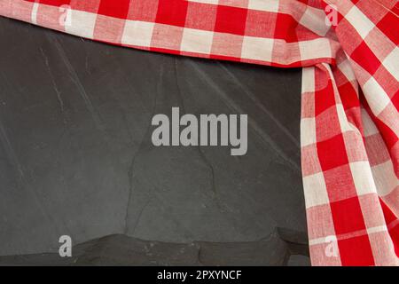 Rotes weißes kariertes Tischtuch auf massivem Schieferteller oder schwarzer Steinhintergrund. Vorlage für Design-Menükarte und Tafel. Speicherplatz kopieren. Oben Stockfoto
