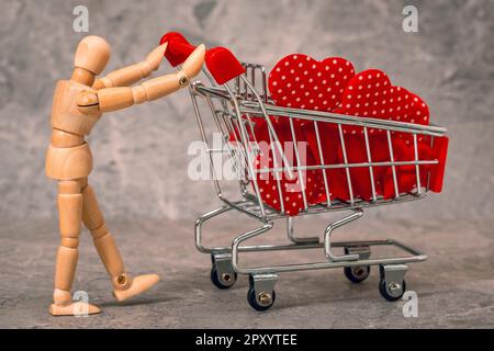 Schaufensterpuppe aus Holz, die einen Einkaufswagen voller Herzen zum Valentinstag schiebt Stockfoto