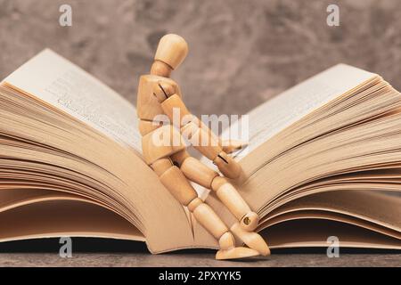 Eine hölzerne Schaufensterpuppe, die auf dem offenen Buch sitzt. Bücher Lesen Zeigt Lernen. Bildungskonzept. Ich liebe das Lesen. Stockfoto