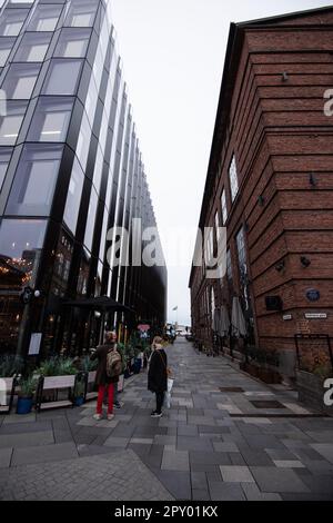 Oslo, Norwegen - Oktober 13 2021: Modernes Glas- und Metallgebäude in Aker Brygge mit Geschäften, Cafés und Büros neben einem traditionellen Backsteingebäude Stockfoto