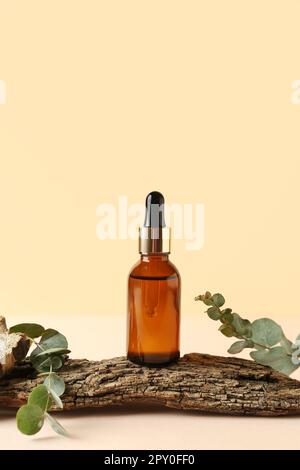 Flasche Kosmetiköl mit Eukalyptusästen und Baumrinde auf blassgelbem Hintergrund Stockfoto