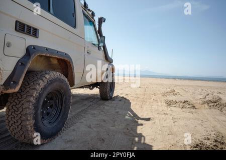 Geländewagen parkt an einem leeren Sandstrand mit Blick auf das Meer. Stockfoto