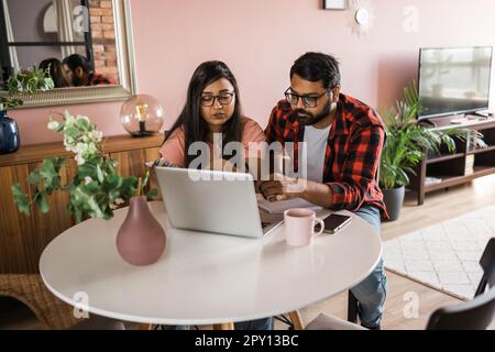 Ernsthafte Ehefrau und Ehemann planen Budget, prüfen Finanzen, fokussierte junge Frau mit Online-Rechner und Zählen von Rechnungen oder Steuern, Mann mit Laptop Stockfoto