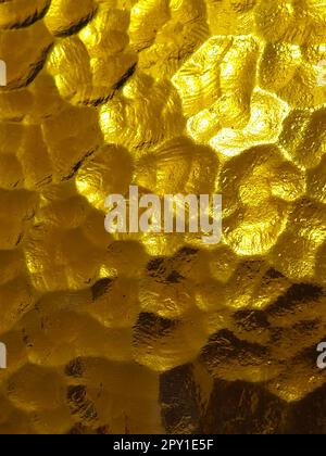 goldgelbes Wellglas mit hellem und dunklem Hintergrund. Lichtreflexionen. Wellglas, Rücklichtquelle. Spiel von Blendung und Reflekti Stockfoto