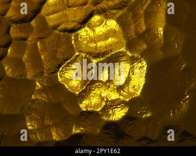 goldgelbes Wellglas mit hellem und dunklem Hintergrund. Lichtreflexionen. Wellglas, Rücklichtquelle. Spiel von Blendung und Reflekti Stockfoto