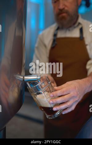 Die Brauerei bietet eine hochwertige Verkostung von Craft-Bier in der Produktionsstätte. Man Brauer gießt frisch gebrühtes Bier oder Lager aus dem Metalltank in Glas Stockfoto