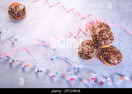 Schokoladen-Berliner-Gebäck für Karneval und Party. Deutsche Krapfen oder Donuts mit Bändern und Konfetti. Farbenfrohes Karneval- oder Geburtstagsbild Stockfoto