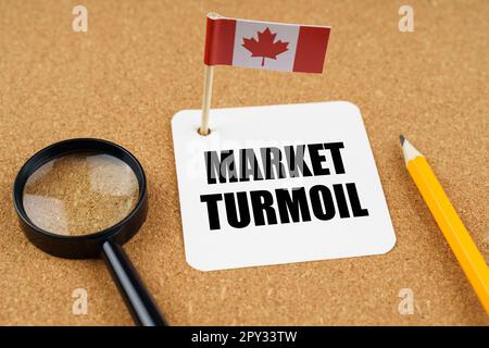 Auf dem Tisch liegt die Flagge Kanadas, ein Bleistift, eine Lupe und ein Blatt Papier mit der Aufschrift - Marktturbulenzen Stockfoto