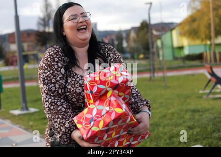 Eine schöne, glückliche junge Frau in Übergröße mit zwei Geschenken, die in einem Park herumläuft Stockfoto