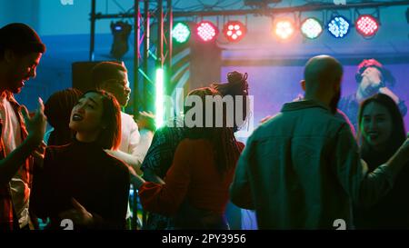 Leute tanzen zu zweit bei langsamer Musik, genießen romantischen Walzer auf der Club-Tanzfläche. Paare, die Spaß auf einer Party mit Scheinwerfern und Bühne haben, feiern zusammen am Abend. Tanzpartner. Stockfoto