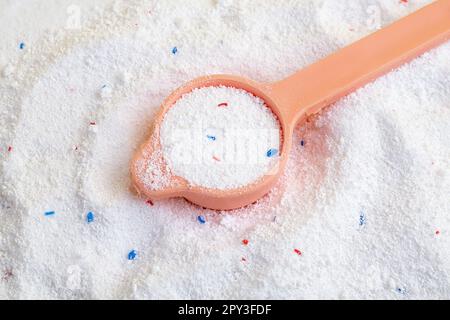 Ein Haufen Waschpulver und ein Messlöffel. Pulver mit blauem und rotem Granulat. Stockfoto