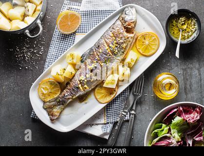 Gebratene traditionelle Flusforelle mit Salat, Kartoffeln und (Knoblauch, Petersilie) Sauce auf grauem Tischhintergrund Stockfoto