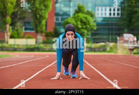 Muslimische Frau in Burka in sportlicher muslimischer Kleidung in Startposition zum Laufen Stockfoto